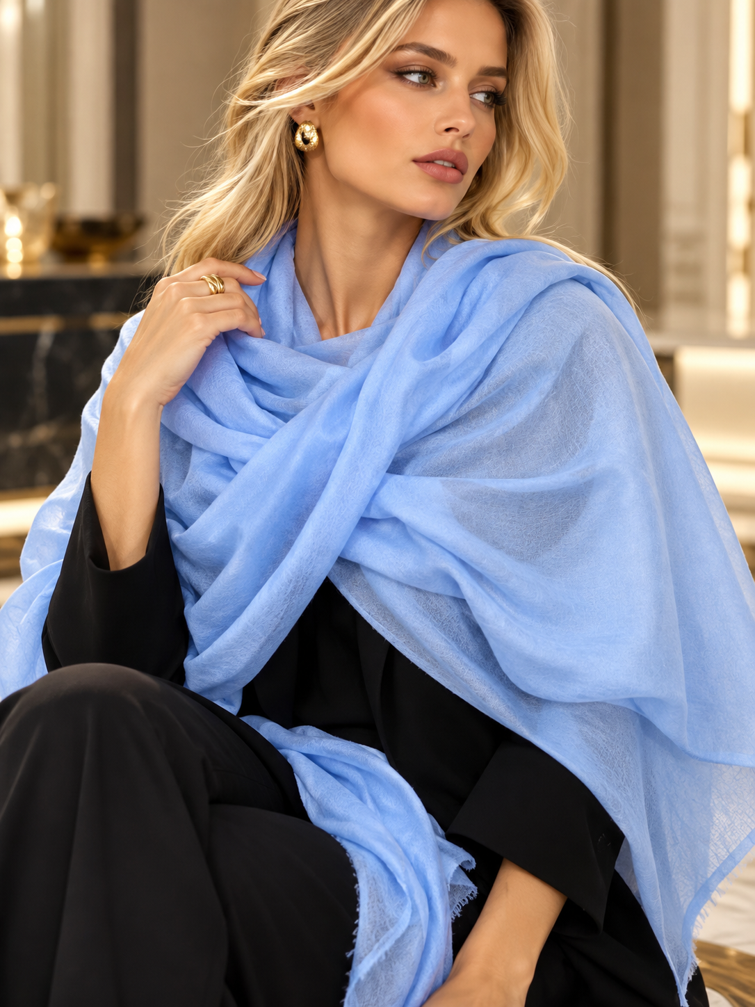A woman wearing a light blue sheer shawl draped over her shoulders, styled over a black outfit in an elegant indoor setting.