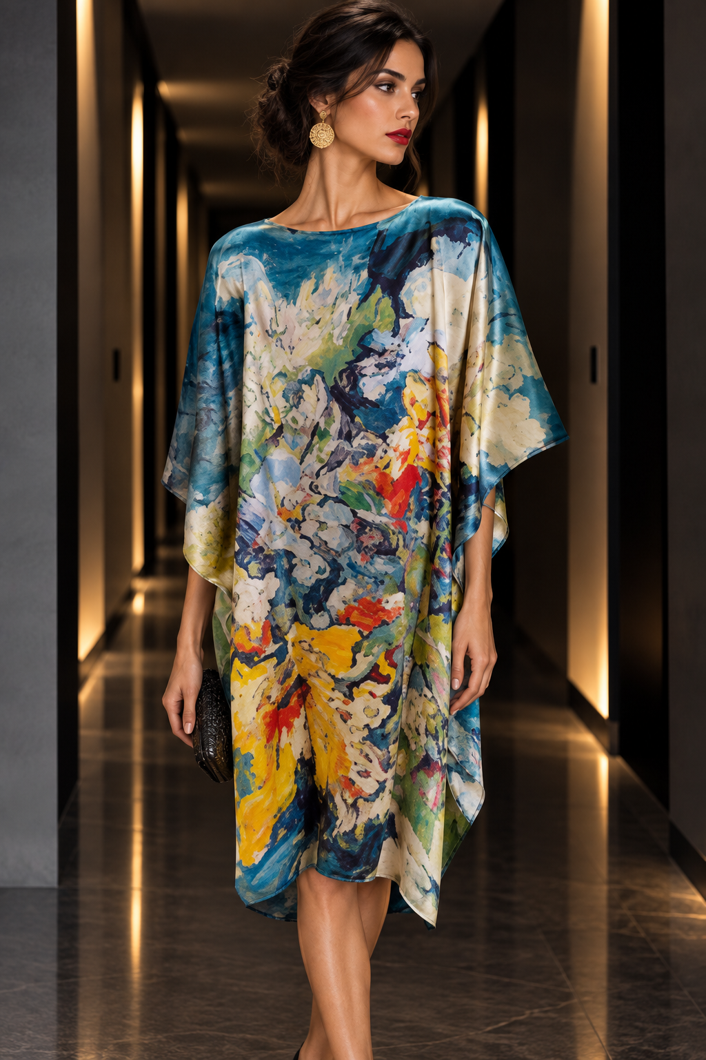 A woman walks down a modern hallway wearing a loose, flowy kaftan dress with a vibrant abstract floral print in blue, yellow, white, and red.