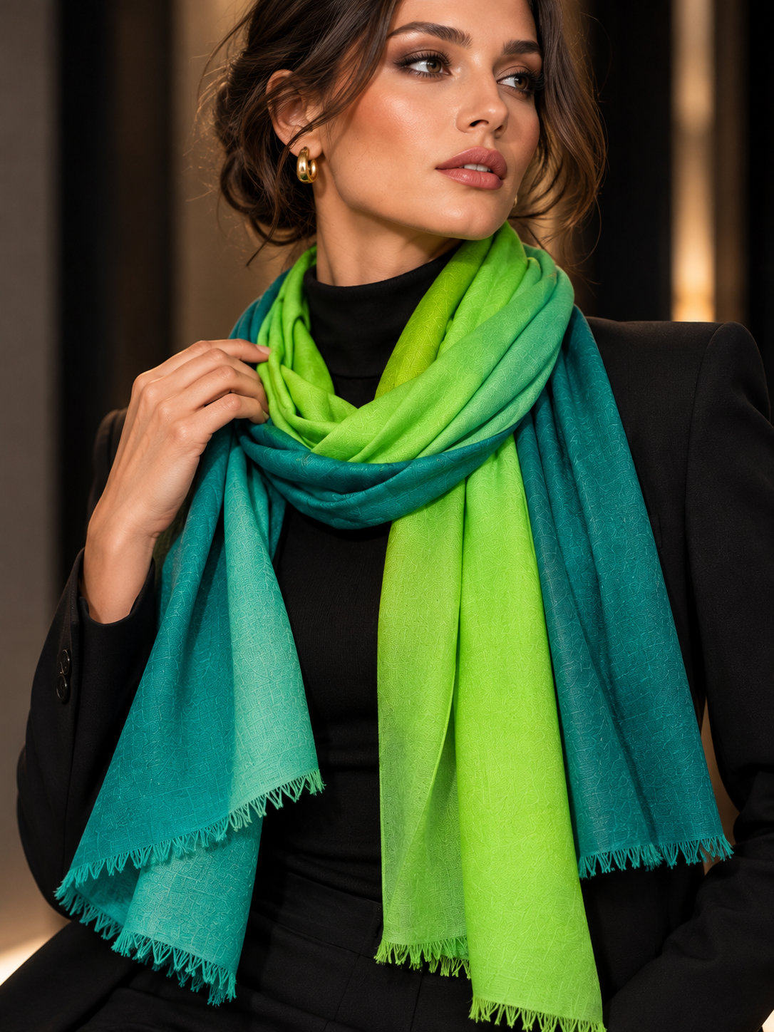 A woman wearing a bright lime green and teal ombre scarf with fringed edges, styled over a black top and blazer.
