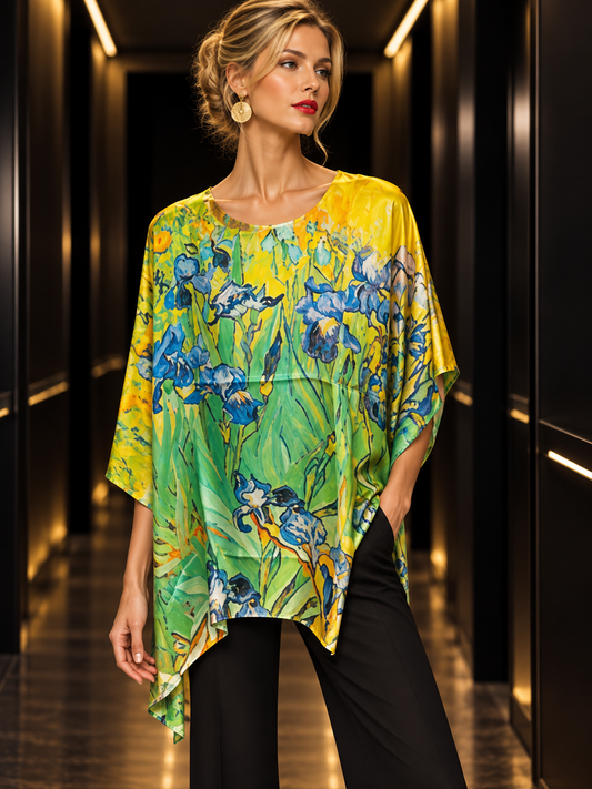 A woman models a vibrant, short-sleeved top featuring a blue and green iris floral print on a yellow and green background, paired with black pants in a dark hallway setting.