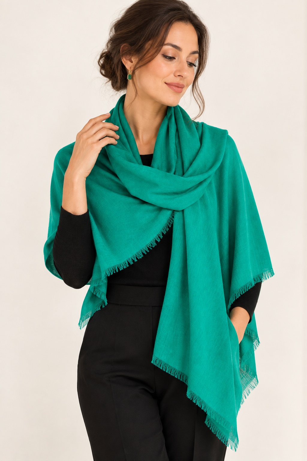 A woman wearing a bright teal-green shawl wrap with fringed edges over a black outfit, photographed against a plain light background.