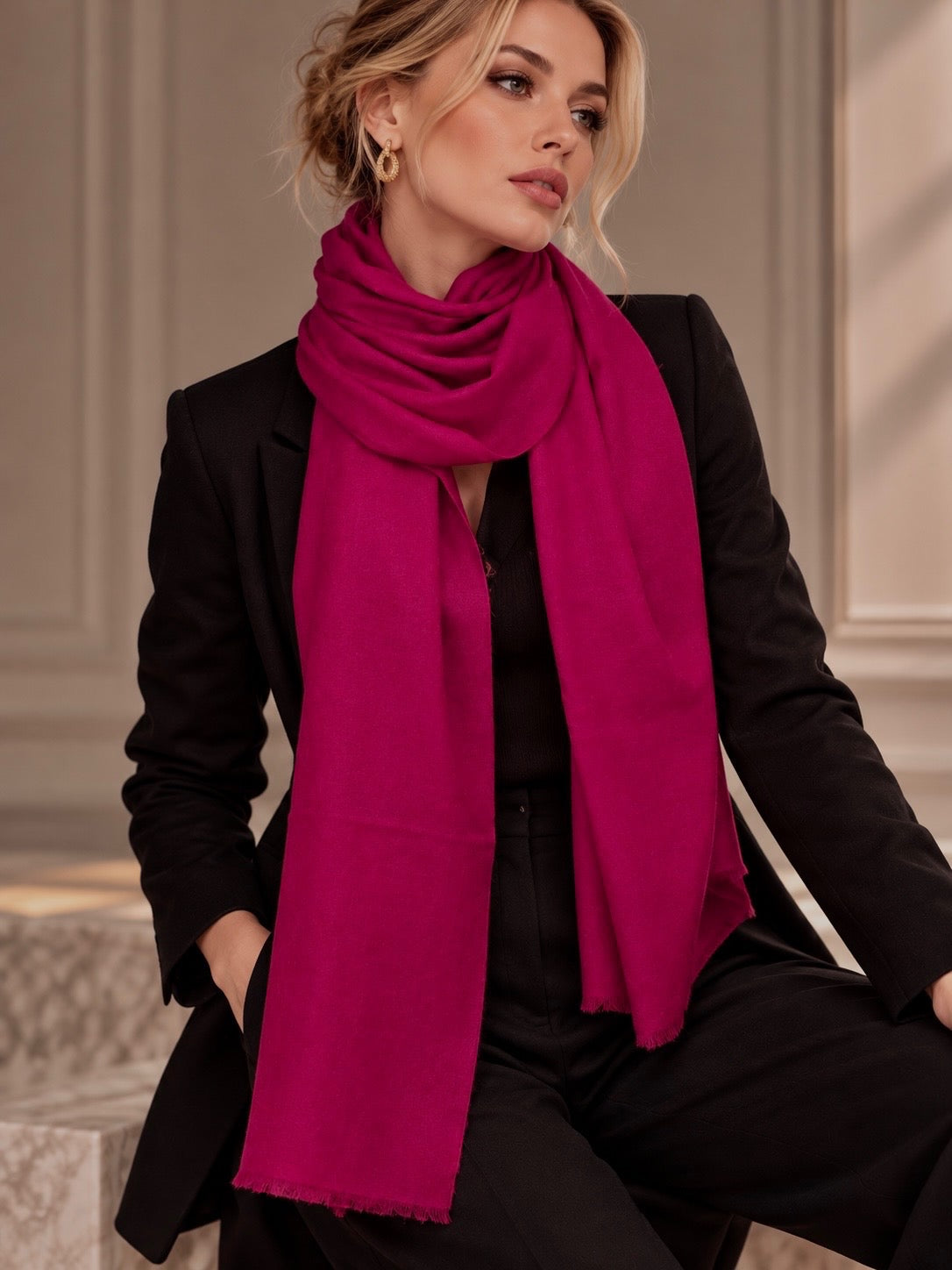 A woman wearing a bright magenta-pink scarf, styled with a black blazer and black pants, posing in an elegant indoor setting.