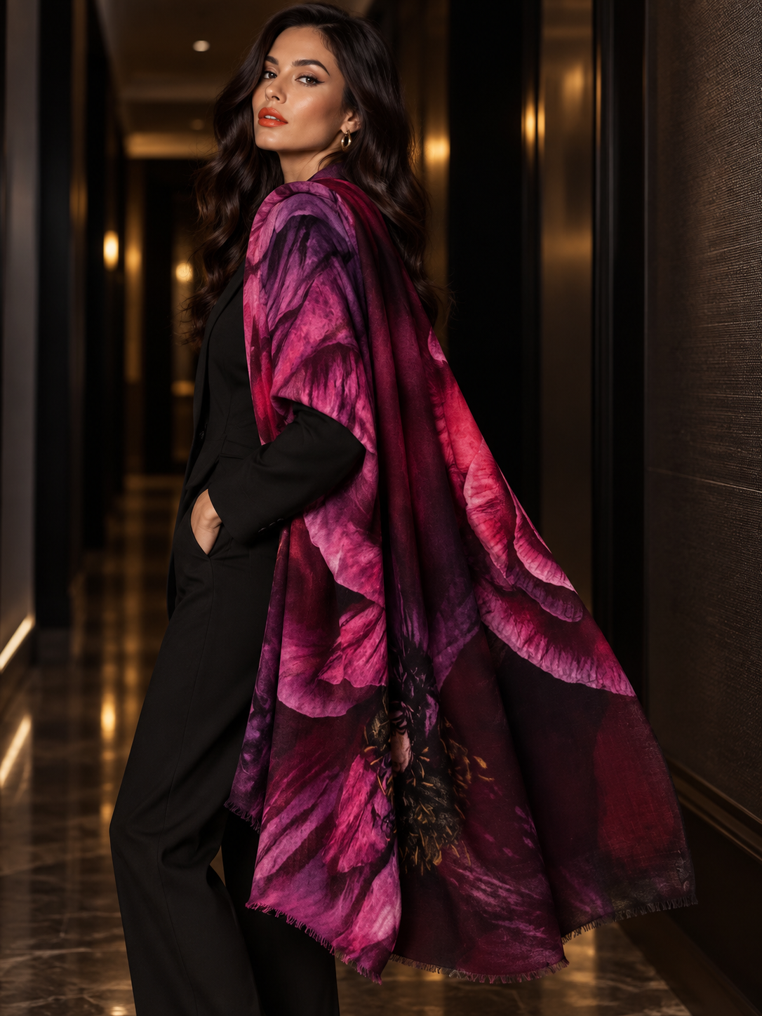 A woman in a black suit stands in a hallway wearing a large, flowing shawl or wrap with a bold floral pattern in deep magenta, purple, and burgundy tones.