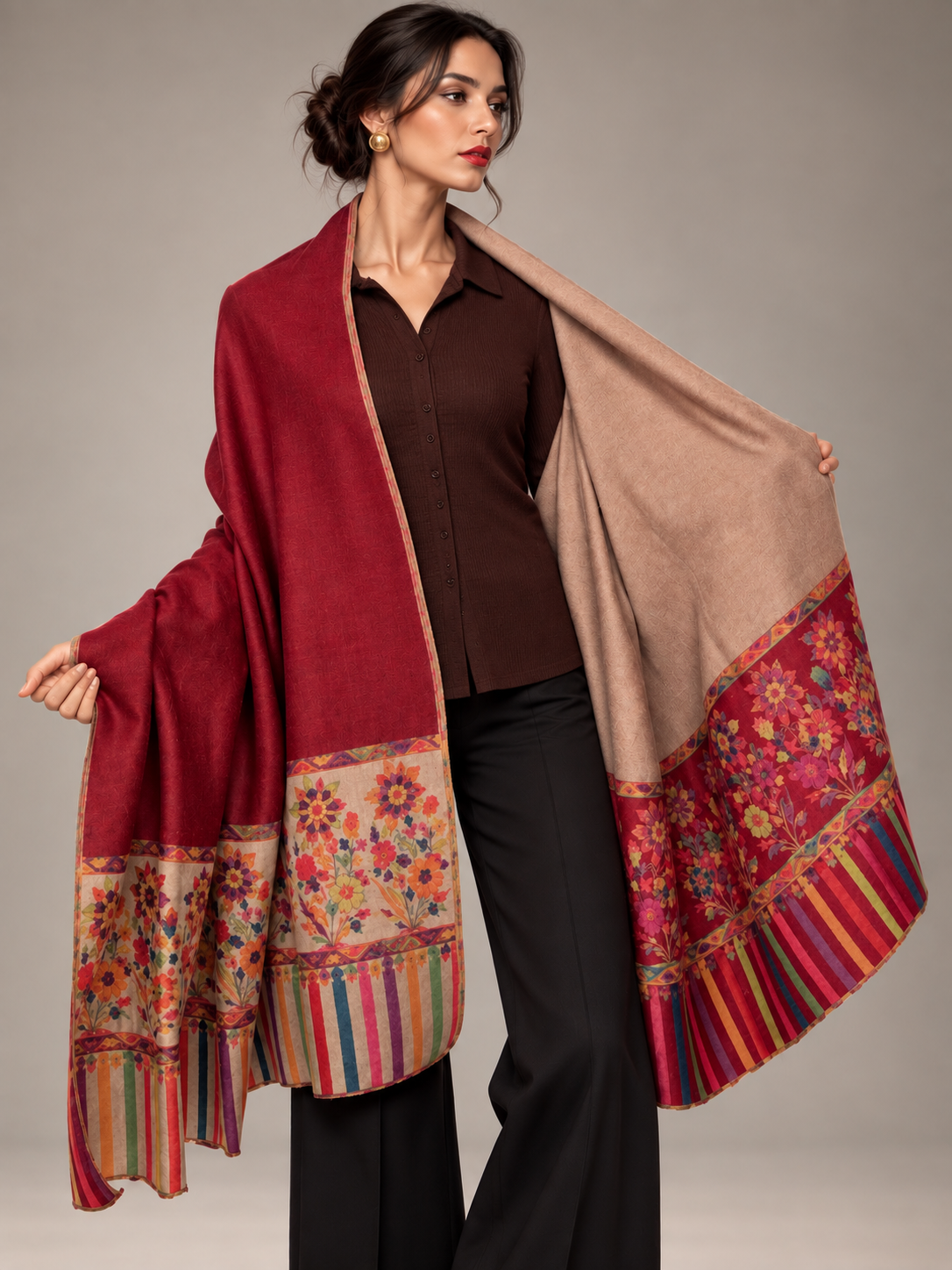 A woman models a luxurious shawl with a deep red body, a beige inner side, and vibrant multicolored floral and striped borders, styled over a dark brown shirt and black pants against a neutral studio background.