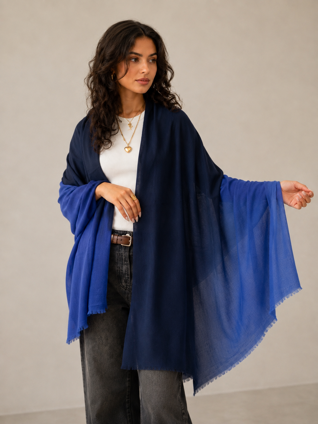 A woman modeling a lightweight navy blue shawl draped over her shoulders, styled over a white top and dark gray jeans against a neutral studio background.