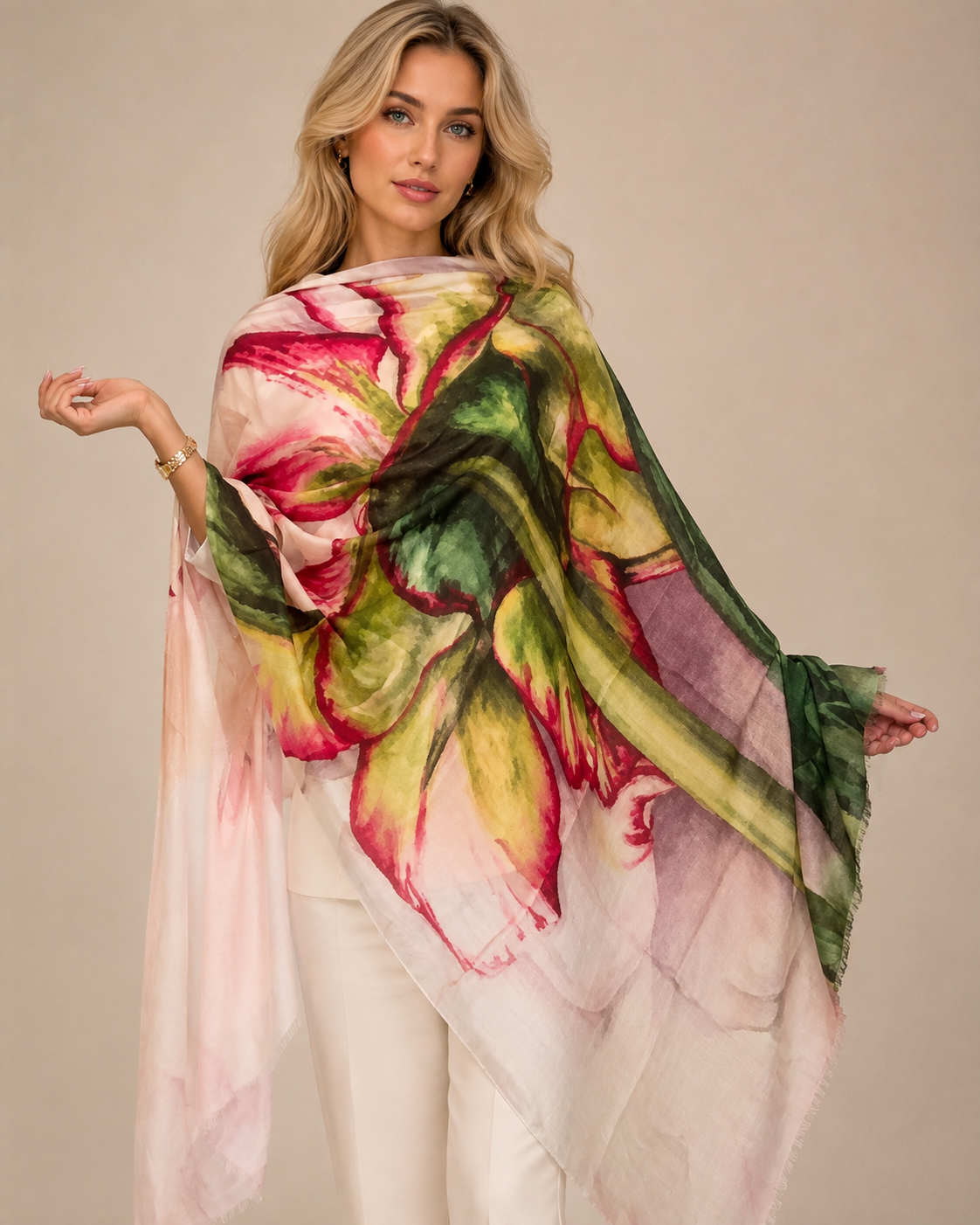 A woman shown from the back wearing a lightweight draped shawl or wrap with a large watercolor-style floral print in red, pink, cream, and olive green, paired with white pants against a plain beige studio background.