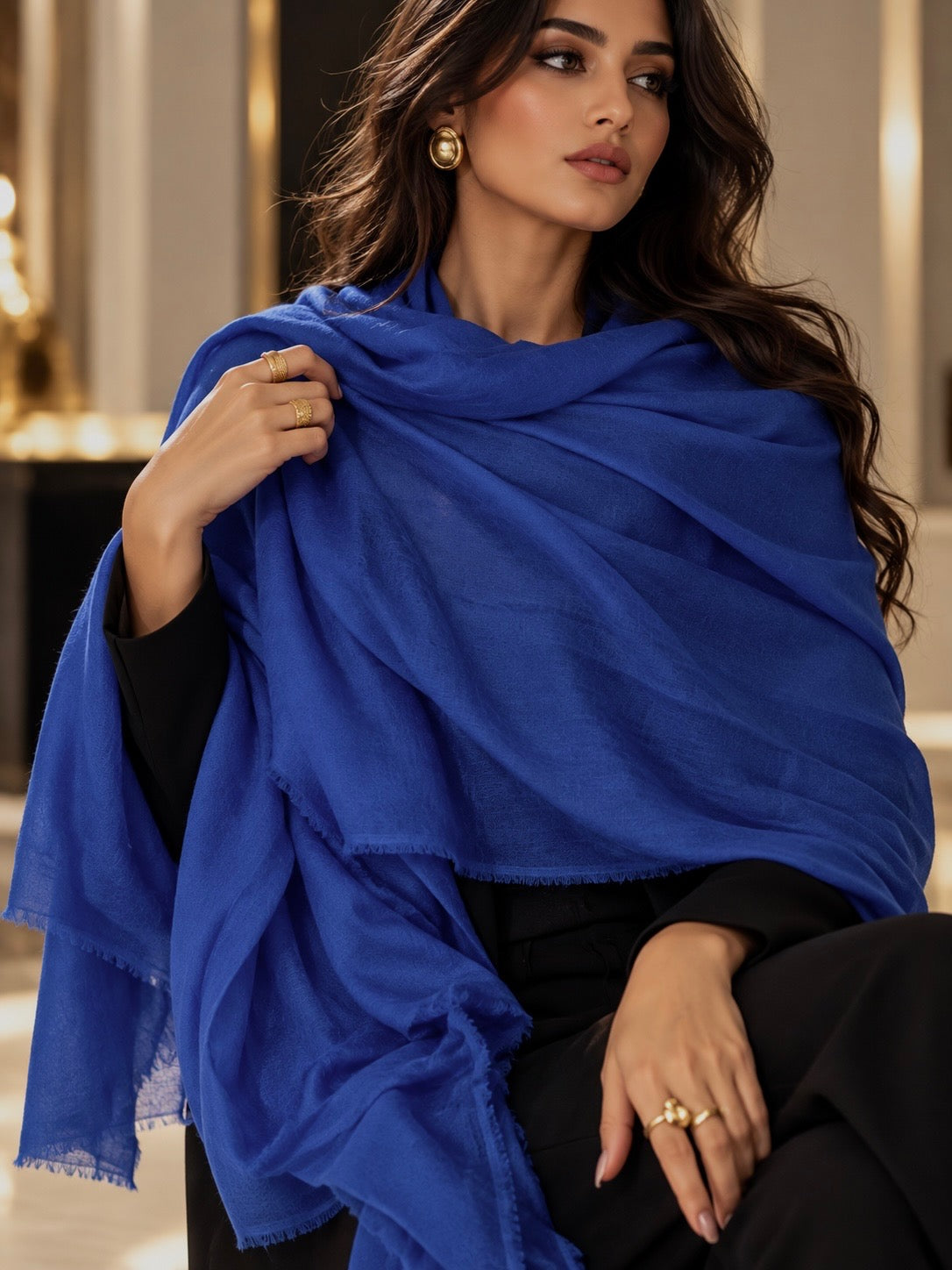 A woman wearing a vibrant royal blue shawl draped over her shoulders, paired with a black outfit, in a softly lit indoor setting.