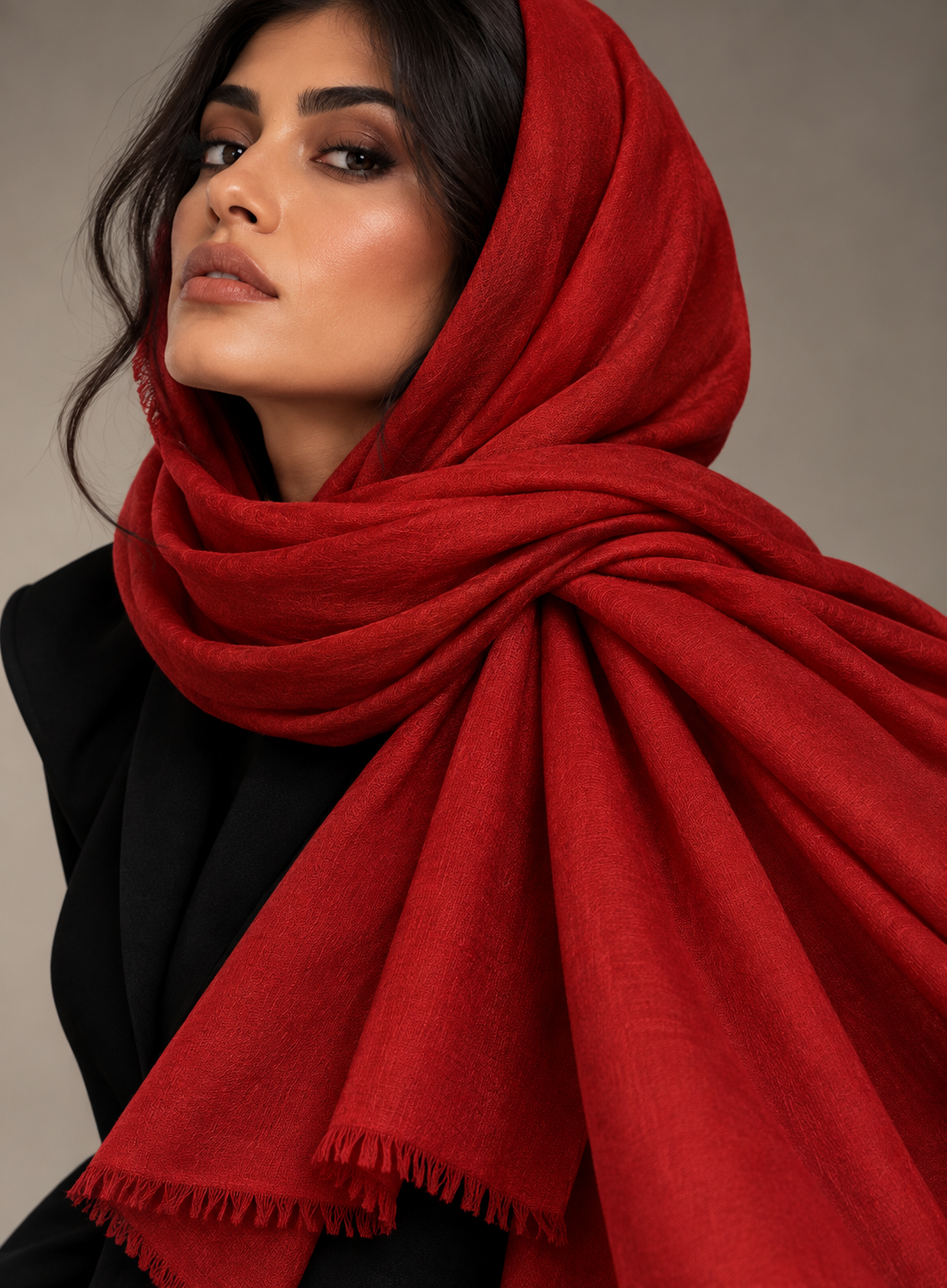 A woman wearing a rich, deep red shawl with fringed edges, styled over a black top against a neutral gray studio background.