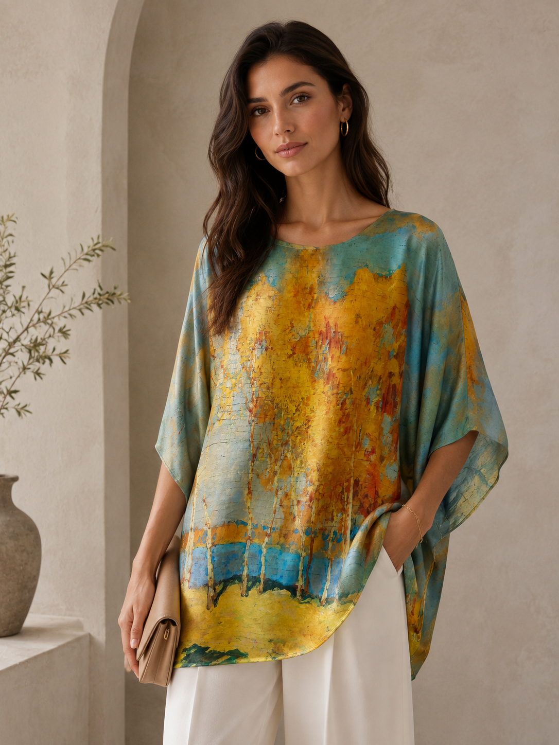 "Printed silk tunic with painterly autumn forest landscape print in golden amber, burnt orange, and sky blue — relaxed batwing fit, editorial editorial shot with clutch"