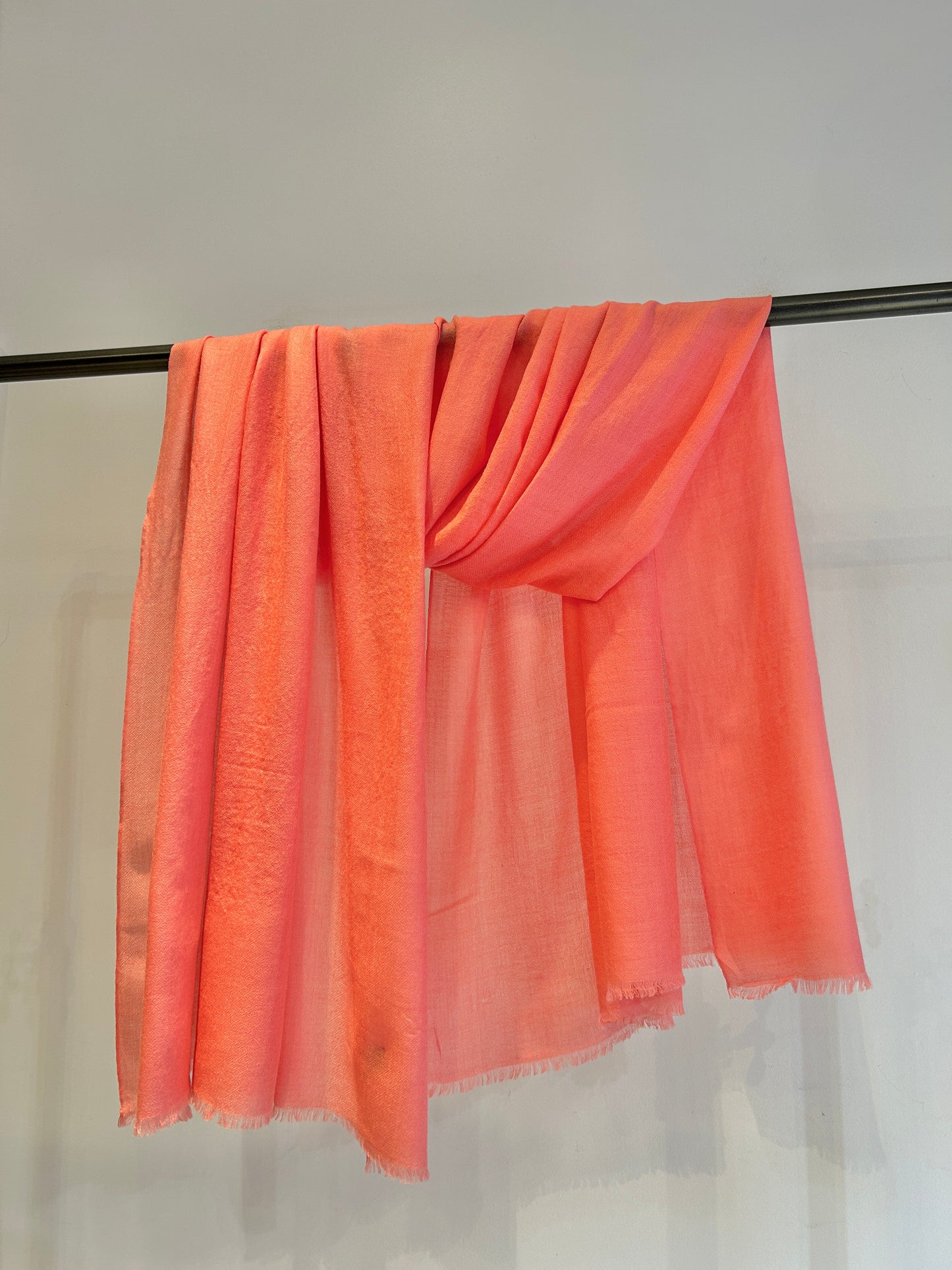Coral-colored scarf draped over a black rod against a white background