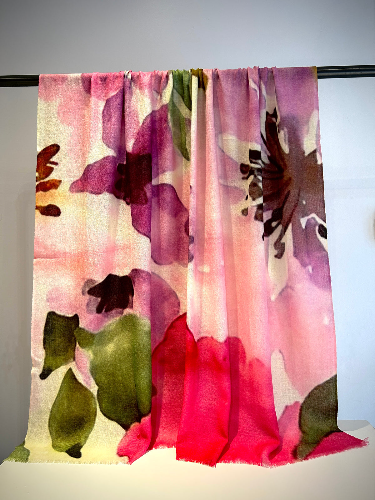 Floral patterned scarf with pink, purple, and green colors on a black rod against a white background.