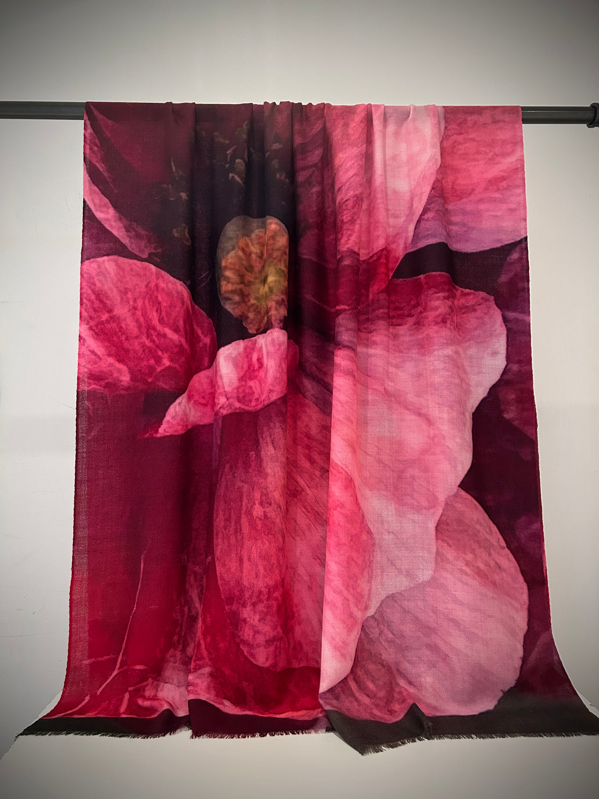Floral patterned shawl handwoven hanging on a rod against a plain background