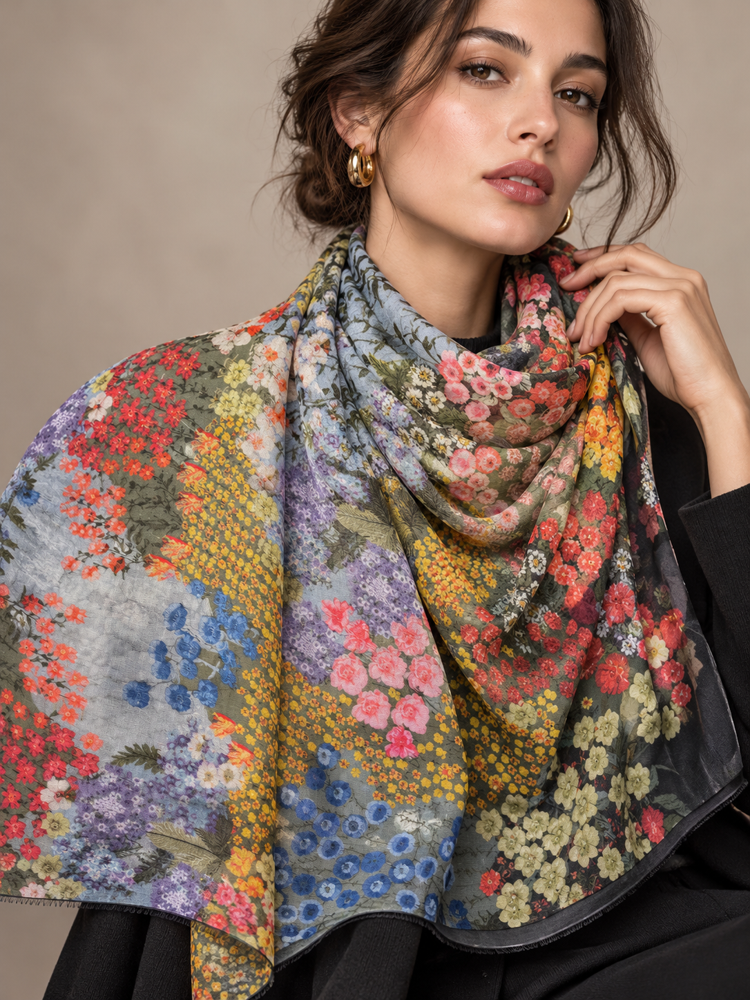 A woman wearing a large multicolor floral scarf with a black border, styled over a black top against a neutral beige background.