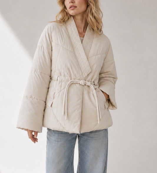 "Transitional quilted kimono-wrap jacket in warm oatmeal beige with shawl collar, rope tie belt, and wide sleeves — worn over blue jeans